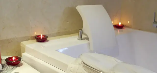Vista de una bañera de hidromasaje blanca empotrada en un baño con paredes de piedra clara.