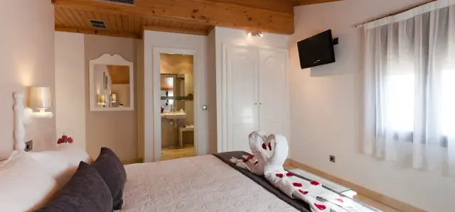 Habitación doble con cama grande vestida de blanco, toalla decorada en forma de cisnes con pétalos rojos, cabecero