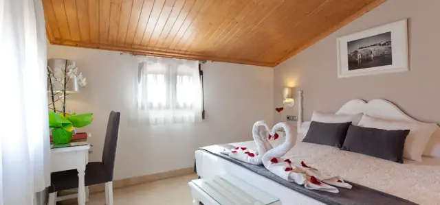 Habitación doble con cama grande vestida en blanco, toallas decoradas en forma de cisnes con pétalos rojos, cabecero
