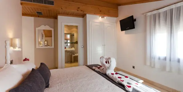 Vista de una habitación doble con cama grande vestida de blanco, toalla decorativa en forma de cisne con pétalos