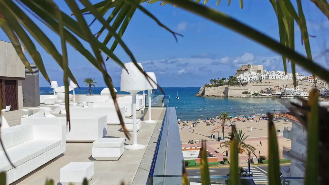 Vista desde una terraza con sofás y sillones blancos hacia la playa, el mar y el castillo de Peñíscola