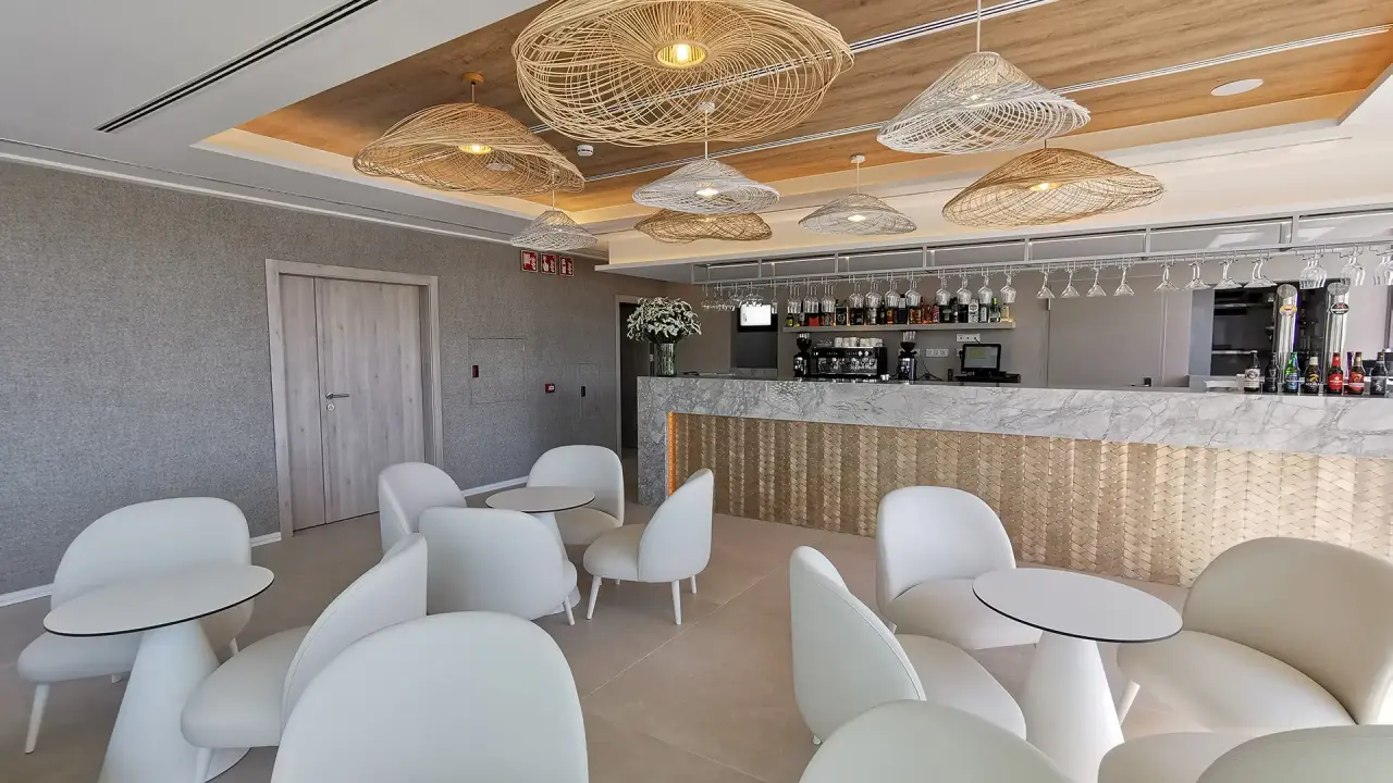 Interior de un espacio de spa con zona de bar, mostrador de mármol, taburetes y sillas blancas modernas, techo