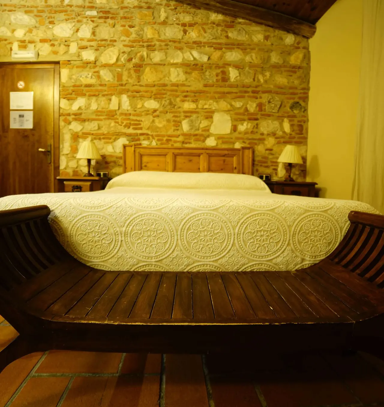 Vista de una suite con cama doble grande cubierta por una colcha blanca con relieve circular, cabecero de madera