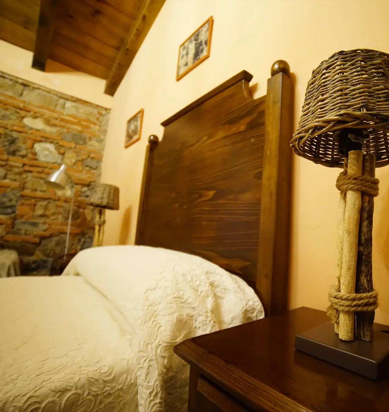Vista de una suite con cama grande de madera oscura, cabecero alto, edredón blanco texturizado, mesita de noche