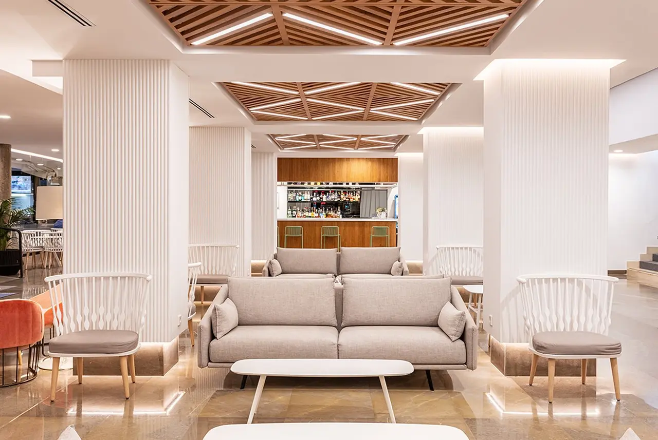 Interior de una sala de estar moderna con un sofá gris central, dos sillones blancos a los lados, una mesa de centro