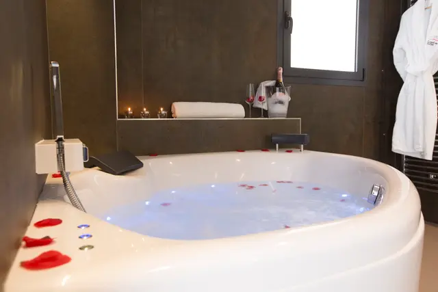 Bañera de hidromasaje redonda blanca en un baño con agua iluminada, pétalos de rosa flotando y bordes.