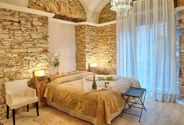 Habitación con paredes de piedra vista, techo abovedado, cama grande con colcha dorada, dos mesitas de noche
