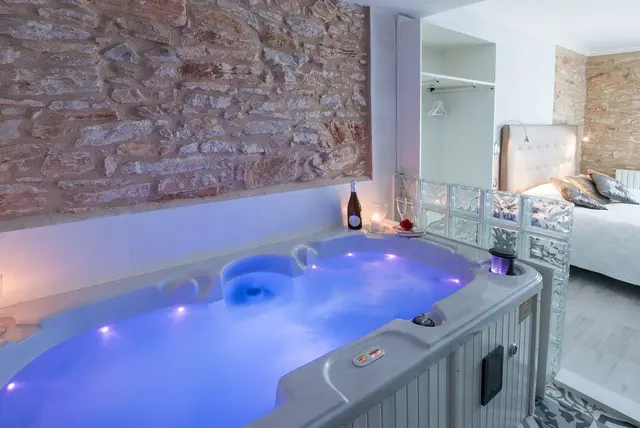 Jacuzzi iluminado con agua burbujeante en un spa privado, junto a una pared de piedra rústica.