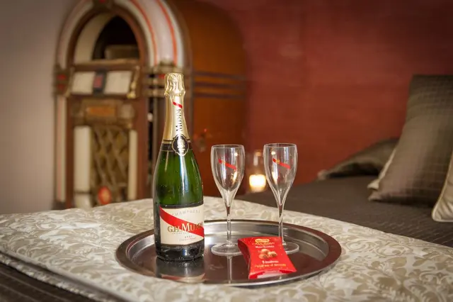 Bandeja plateada sobre una cama con una botella de champán Moët & Chandon, dos copas de flauta y un pequeño paquete