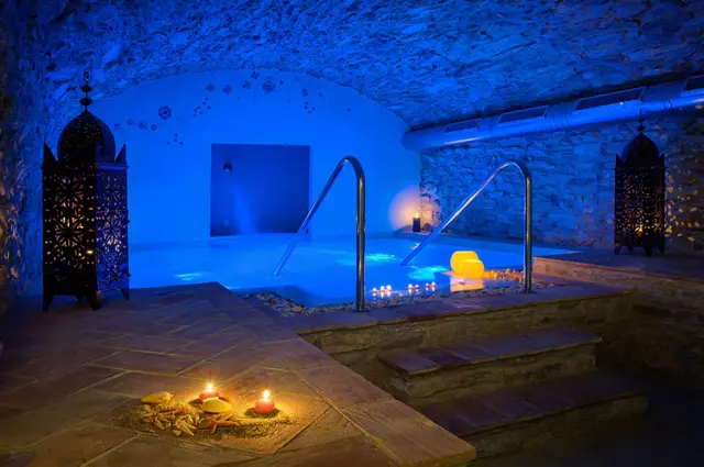 Vista de un spa privado con piscina interior iluminada en tonos azules, ubicada en una cueva de piedra con techo