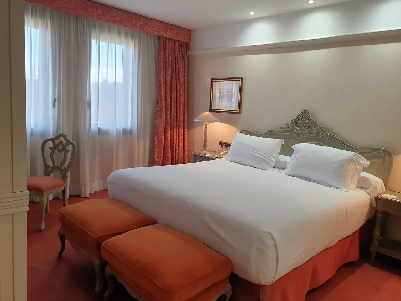 Vista de una suite ejecutiva junior con una gran cama doble con cabecero ornamentado, dos cojines naranjas a los pies