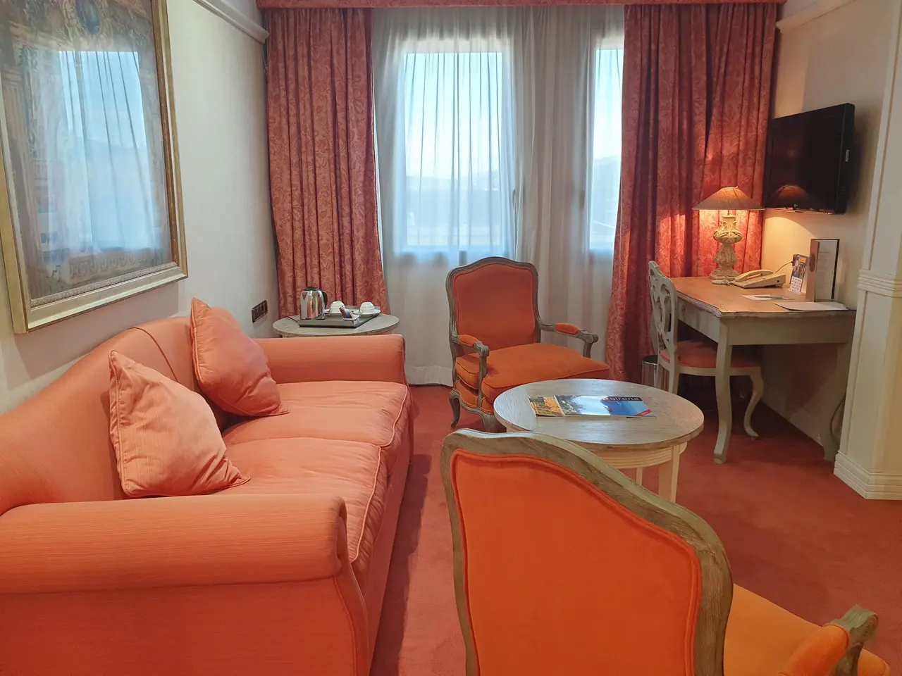 Vista de una sala de estar en una suite ejecutiva junior con sofá naranja de dos plazas, sillones y sillas a juego