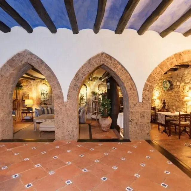 Interior de una suite con arcos de piedra, suelo de terracota y techos con vigas de madera pintadas de azul.