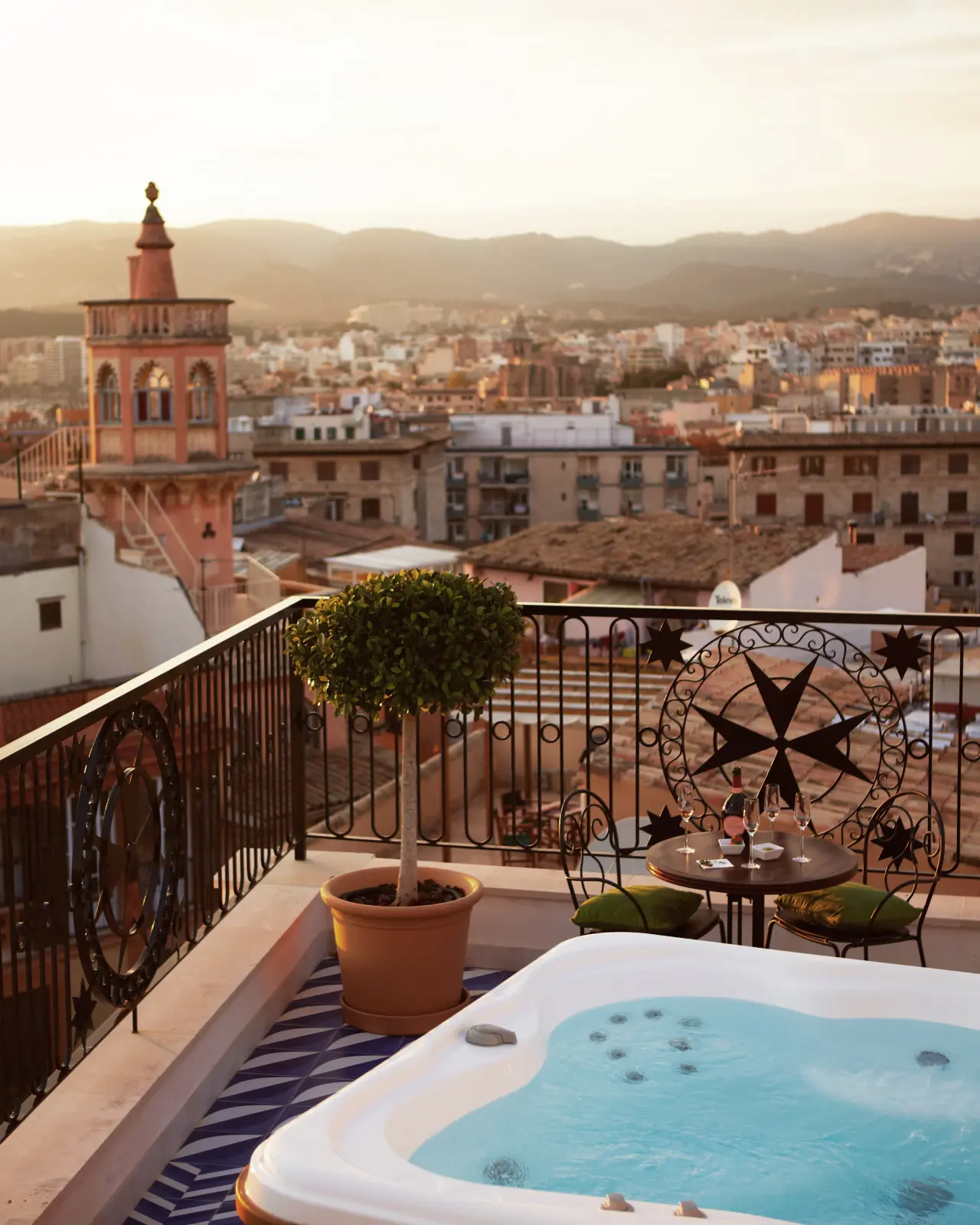 Jacuzzi en terraza privada con vistas a la ciudad y montañas al atardecer.