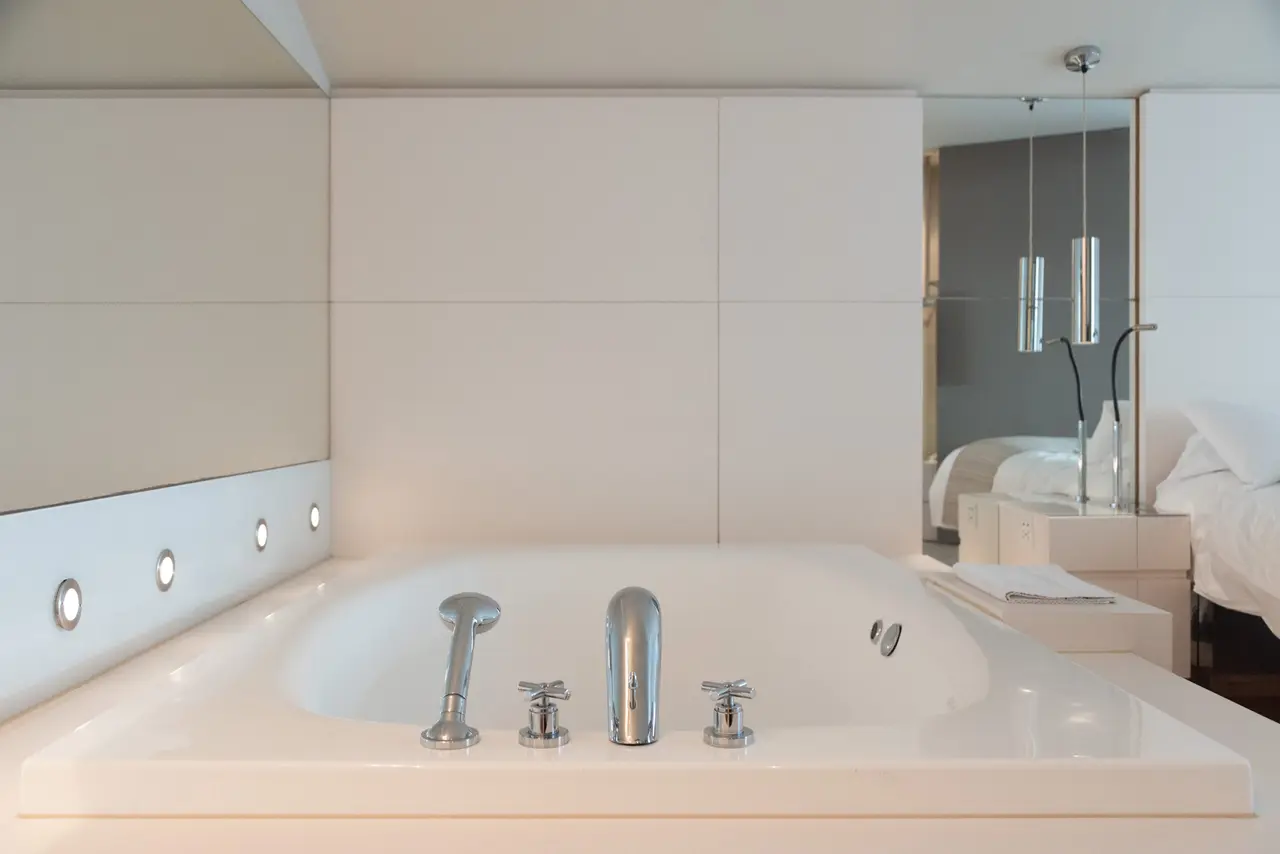 Bañera de hidromasaje blanca rectangular empotrada en una suite, con grifería cromada, luces LED en el borde y vista