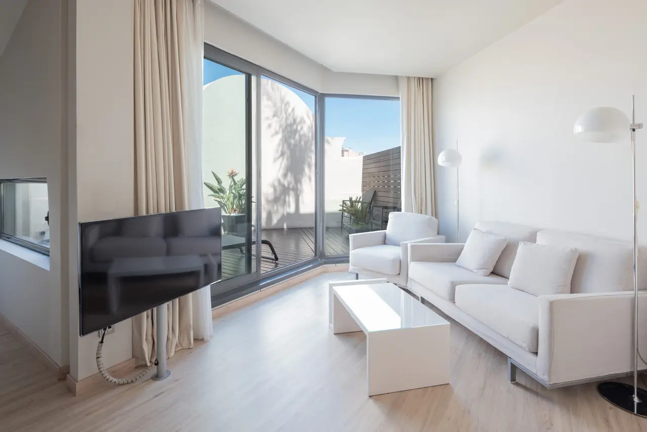 Interior de una suite con paredes blancas y suelo de madera clara. A la izquierda, un televisor montado en la pared.