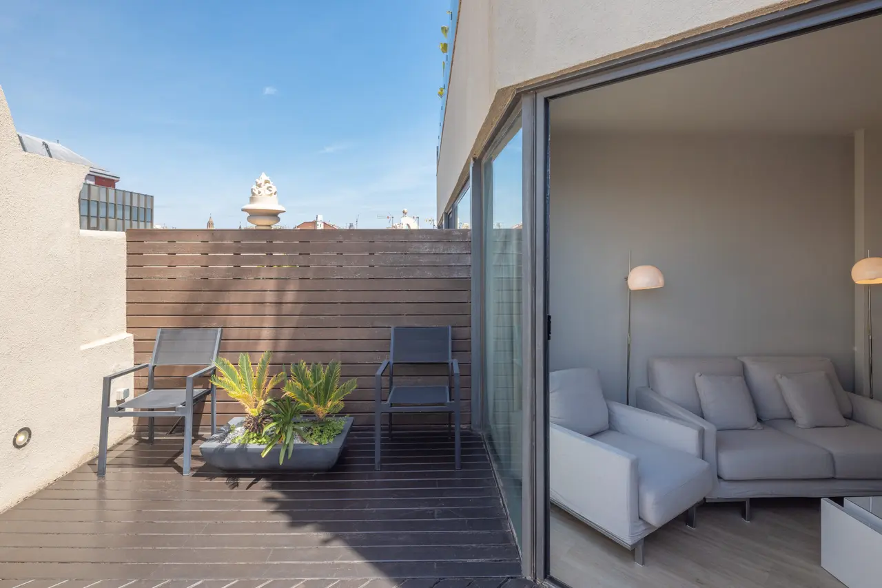 Terraza privada de una suite con suelo de tarima oscura, dos sillones grises, una mesa rectangular con plantas
