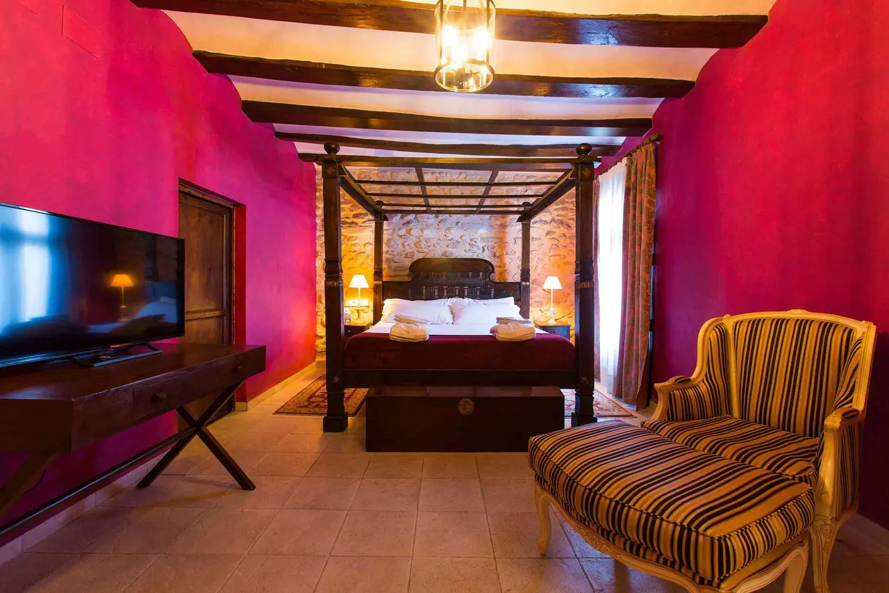 Habitación con paredes pintadas de color rosa intenso, techo con vigas de madera oscuras, cama de dosel grande
