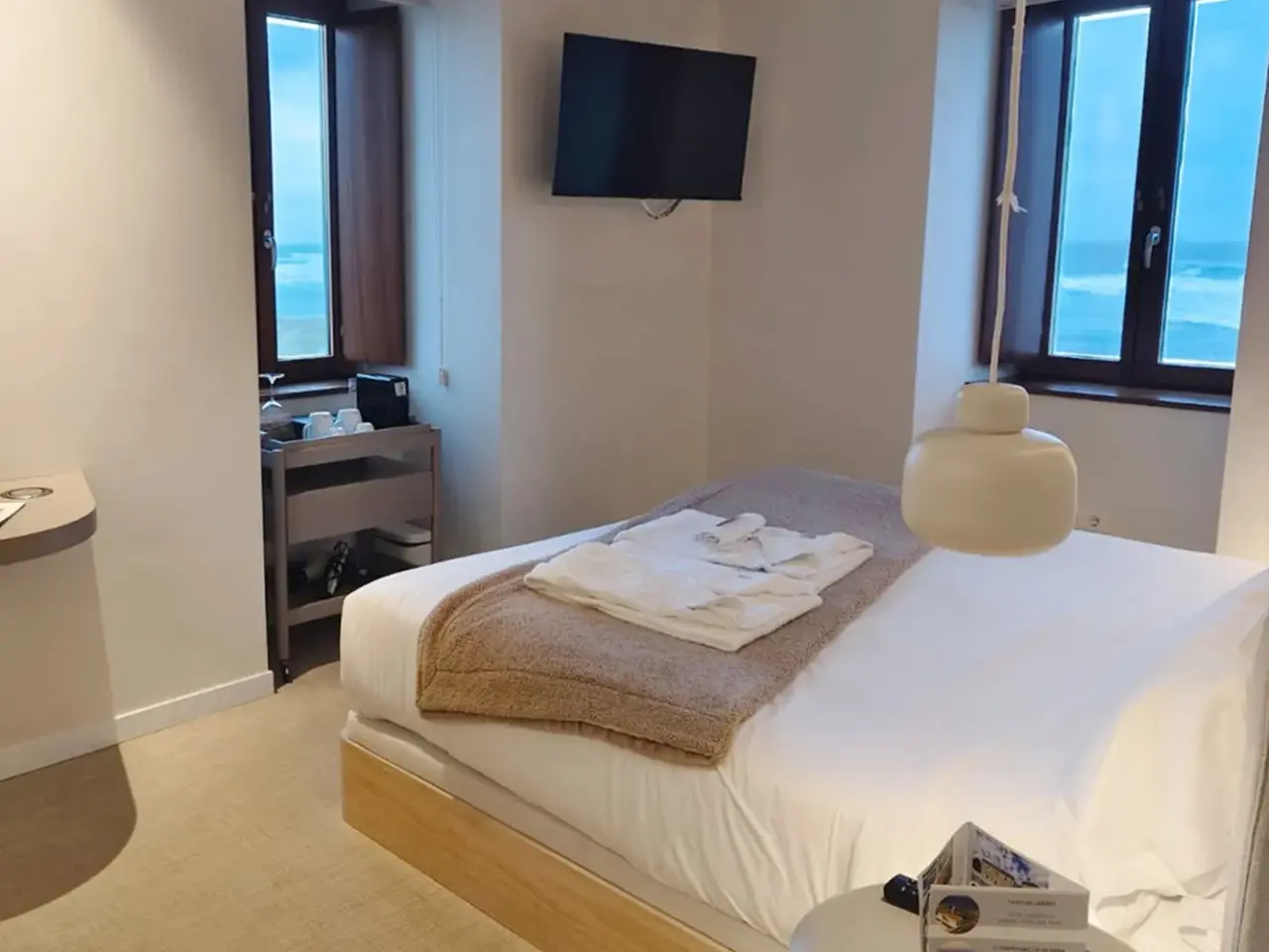 Habitación de hotel con cama doble vestida con sábanas blancas y una manta marrón, televisión montada en la pared