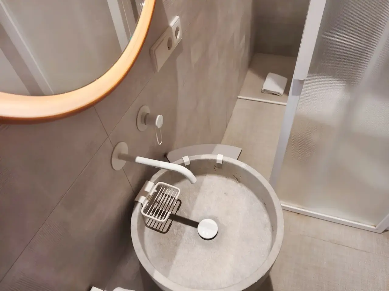 Bañera de hidromasaje redonda de piedra clara con grifo blanco, soporte para jabón y desagüe central, instalada