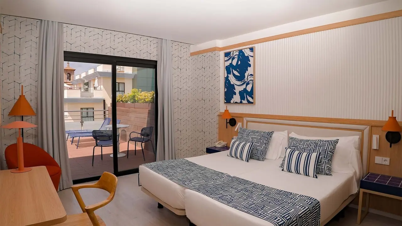 Vista de una junior suite de hotel con cama doble grande vestida con sábanas blancas y cojines de rayas azules