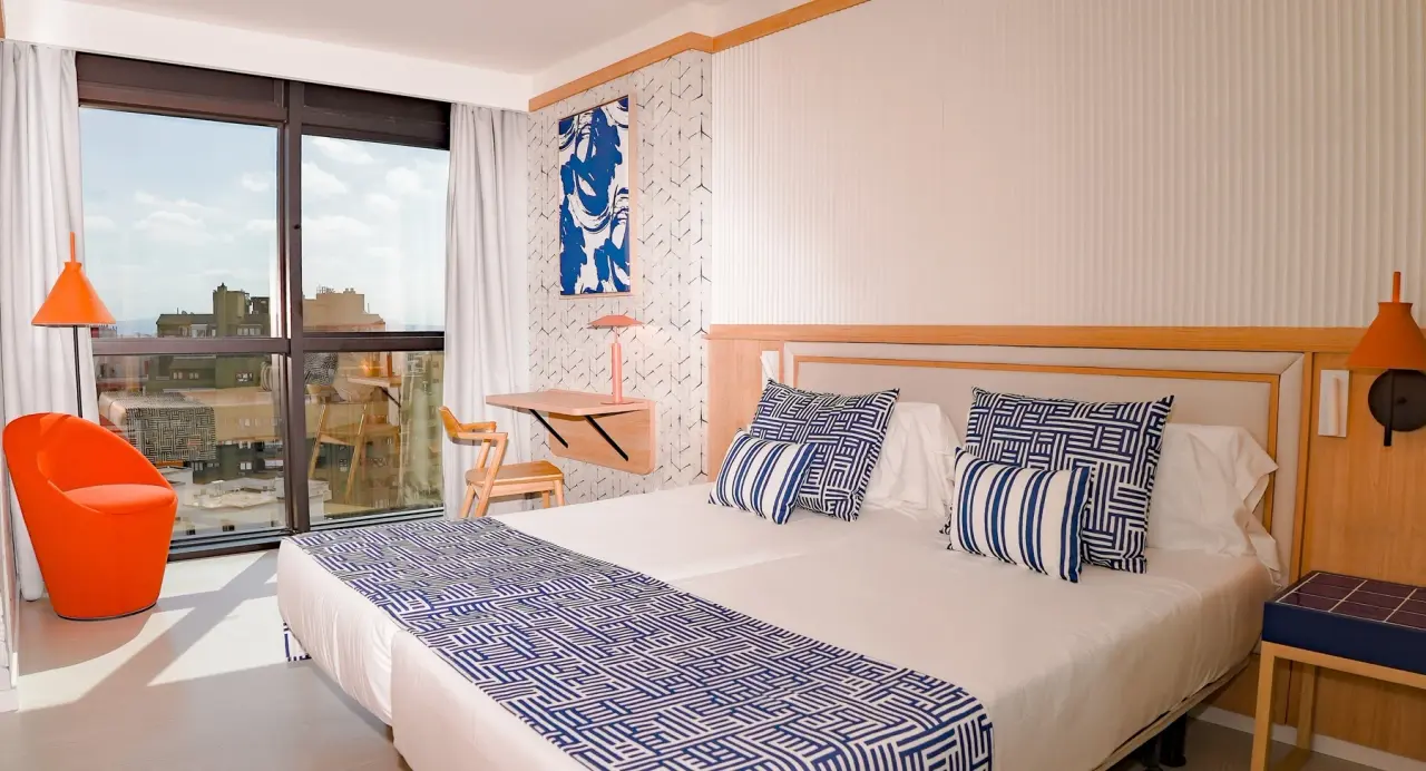 Vista de una junior suite con cama doble, cabecero de madera, almohadas y cojines con estampados azules y blancos
