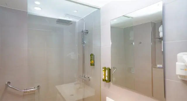 Baño de suite con ducha de mampara de vidrio, grifería cromada, barra de apoyo, espejo grande y dispensadores