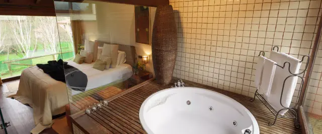 Jacuzzi redondo blanco empotrado en una plataforma de madera, con grifos metálicos y jets visibles. Detrás hay una pared