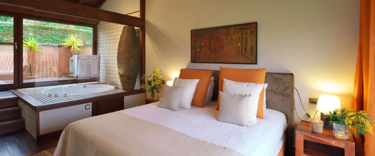 Habitación de hotel con cama doble vestida de blanco y naranjas, mesitas de noche con lámparas encendidas