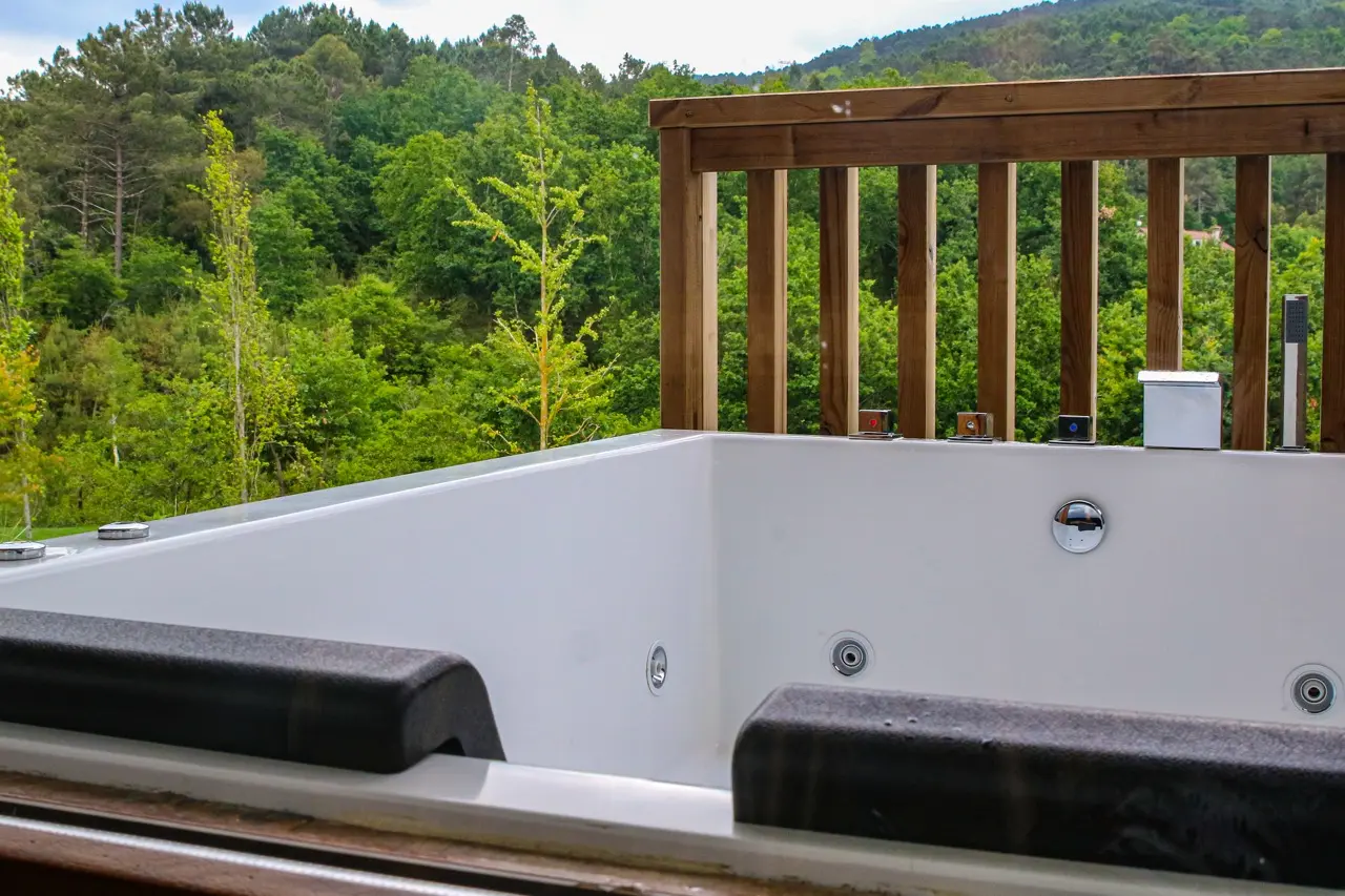 Bañera de hidromasaje exterior privada con barandilla de madera y vistas al bosque.