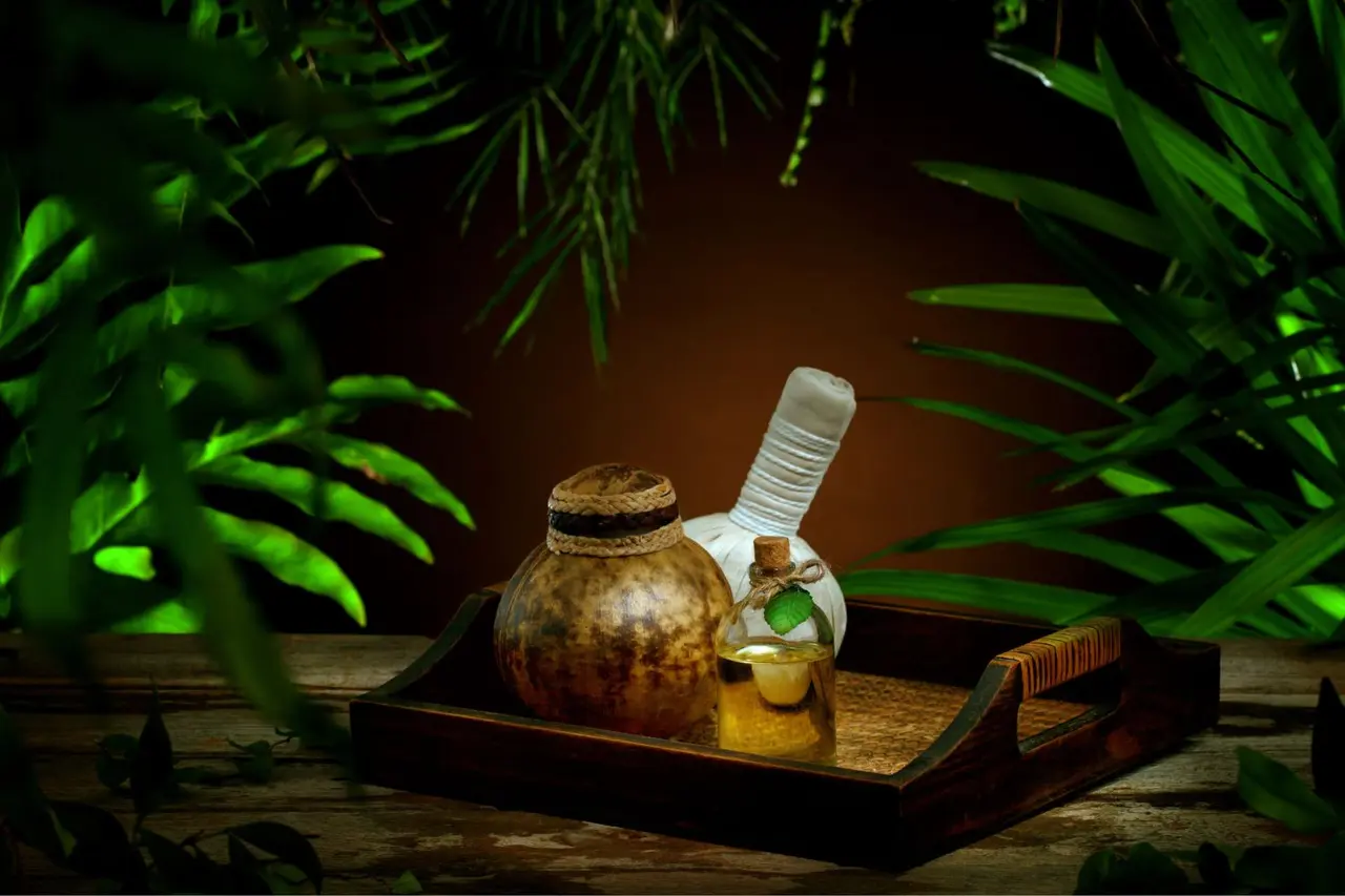 Bandeja de madera con accesorios de spa sobre una superficie de madera, rodeada de hojas verdes de plantas.