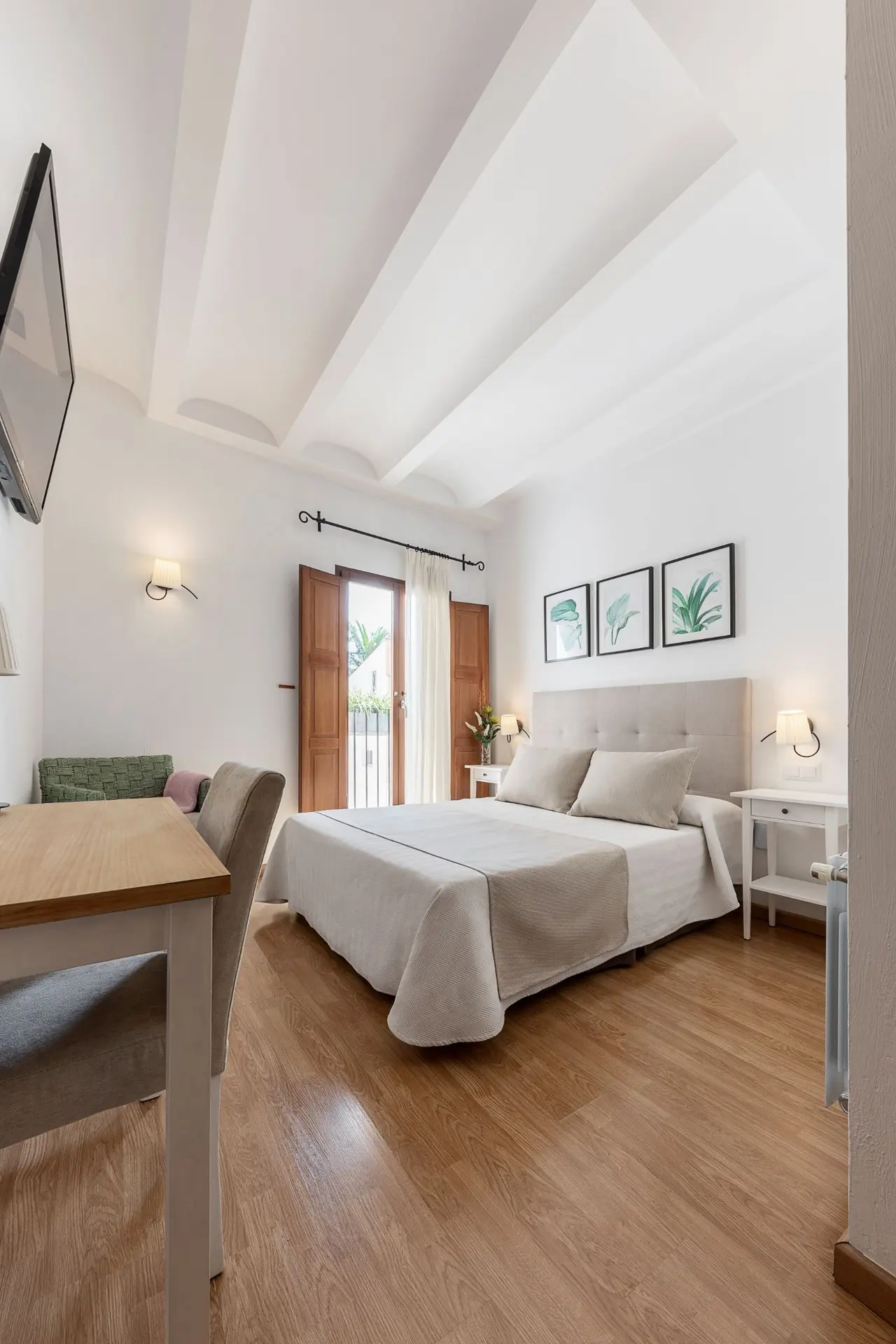 Habitación de hotel con cama doble, cabecero beige, mesitas de noche con lámparas, suelo de madera clara, mesa