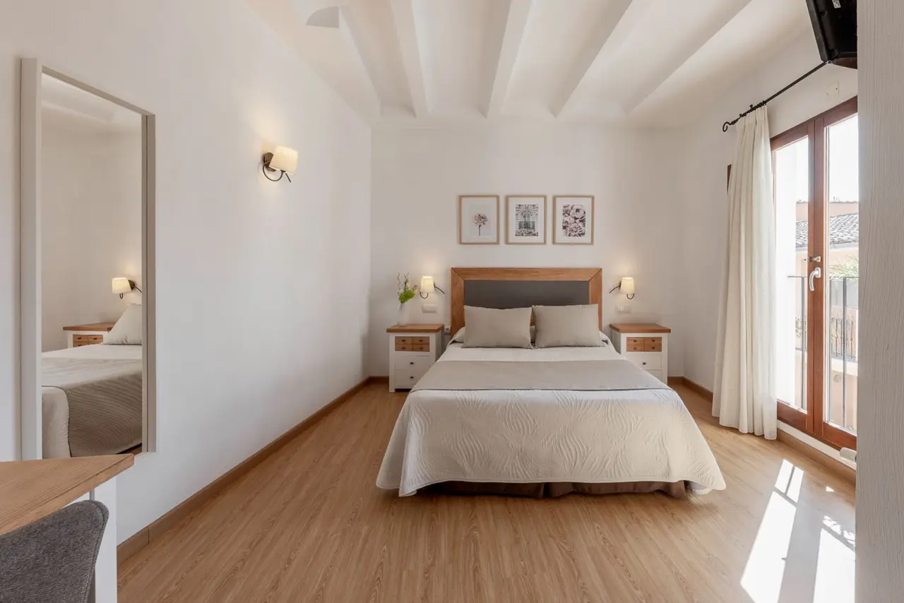 Habitación de hotel con cama doble, cabecero de madera, mesitas de noche, espejo de cuerpo entero a la izquierda