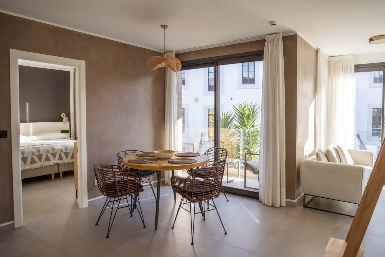 Interior de una habitación con zona de comedor que incluye una mesa redonda de madera y cuatro sillas de mimbre