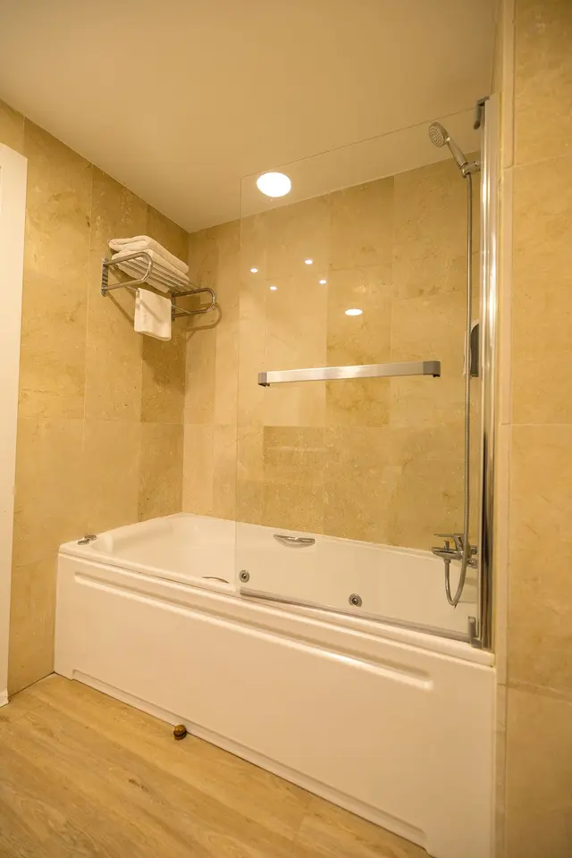 Baño con bañera blanca de hidromasaje, mampara de cristal, ducha con alcachofa y manguera flexible, toallero