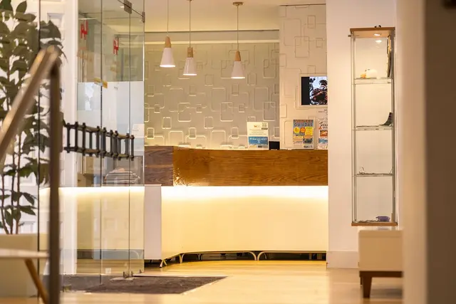 Recepción de hotel con mostrador de madera iluminado, pared decorativa con patrones geométricos, lámparas colgantes