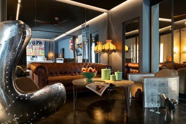 Salón de hotel con sillones de cuero, mesa de centro y decoración moderna con espejos y luces cálidas.