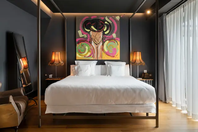 Dormitorio de suite con cama king size blanca, cabecero de cuatro postes, gran cuadro colorido en la pared