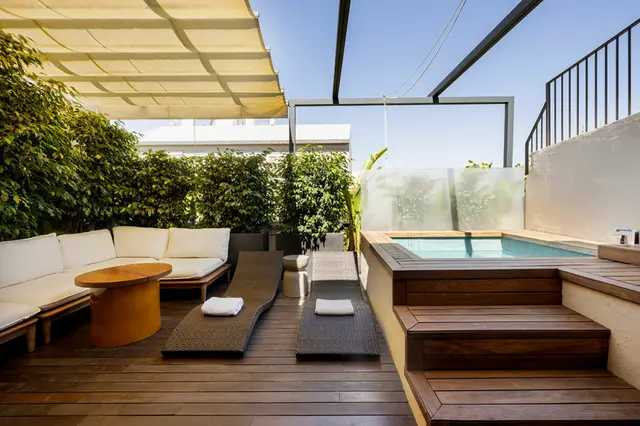 Terraza privada con jacuzzi rectangular, dos tumbonas, sofá exterior y pérgola bajo un cielo despejado.