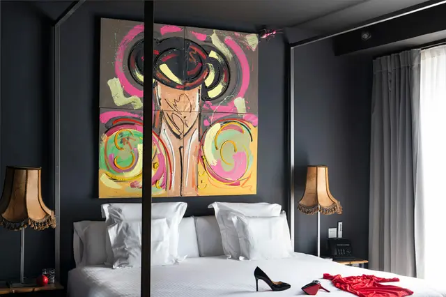 Dormitorio de suite con cama blanca, arte abstracto colorido en la pared oscura y ventana con cortinas.