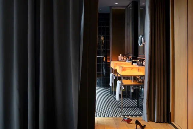 Vista a un baño moderno con doble lavabo de piedra iluminado, toallas colgadas y suelo de mosaico, visto