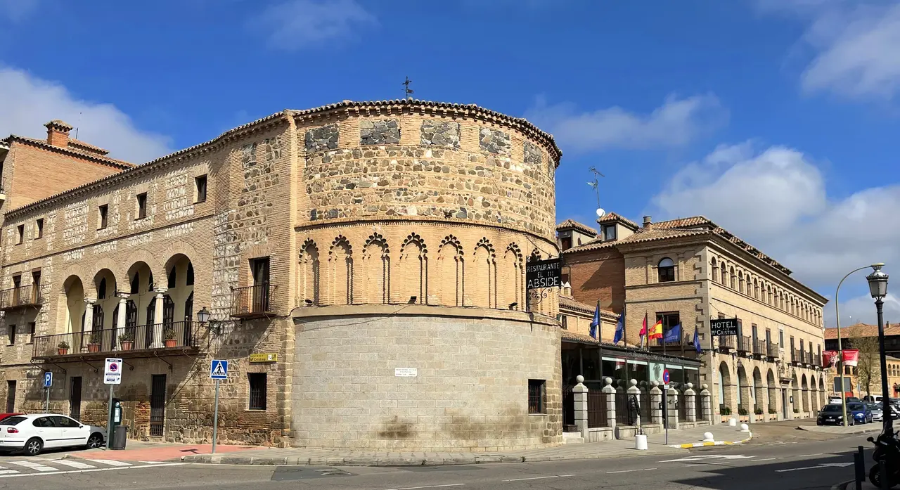 Vista exterior de un edificio histórico de piedra con forma curva y arcos, ubicado en una calle urbana con otros