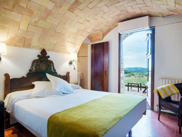 Habitación con cama doble, cabecero de madera tallada, colcha verde, techo abovedado de ladrillo visto y puerta