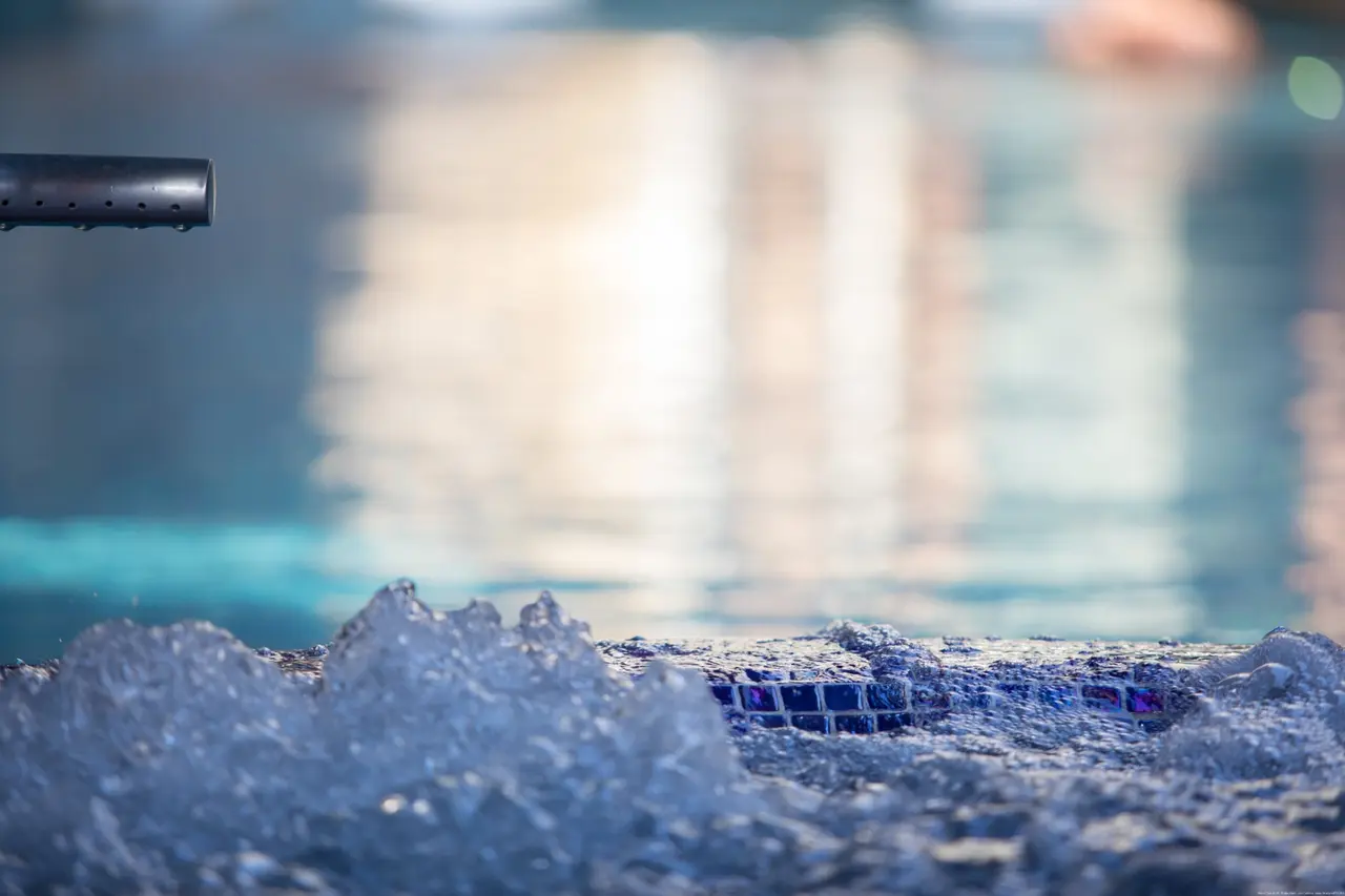 Detalle de un spa nocturno con agua burbujeante iluminada en tonos azules, borde de mosaico y un chorro de agua