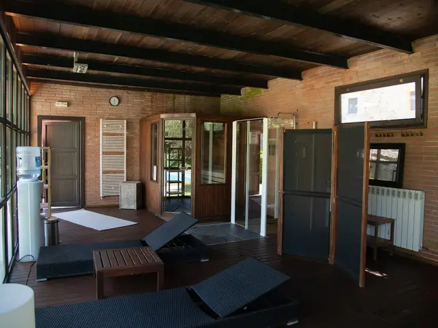 Interior de un spa privado con suelo de madera, techo con vigas oscuras, paredes de ladrillo visto, dos tumbonas
