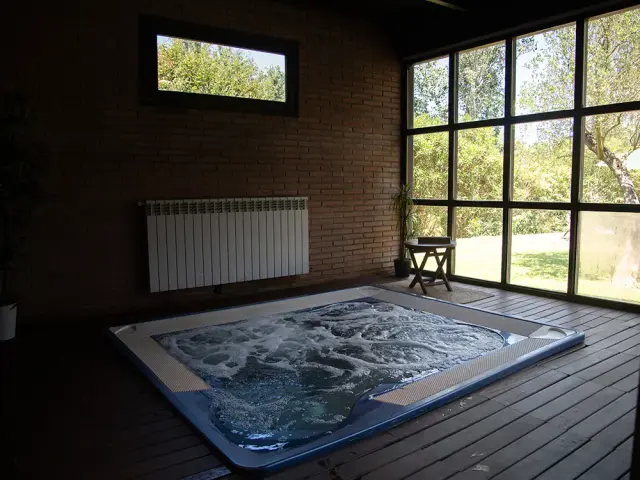 Spa privado en una habitación con paredes de ladrillo visto, suelo de madera, gran ventana con vistas al exterior