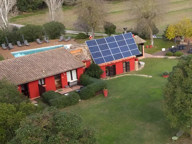 Vista aérea de una casa rural roja con tejado de teja, paneles solares en el tejado, piscina rectangular y zona