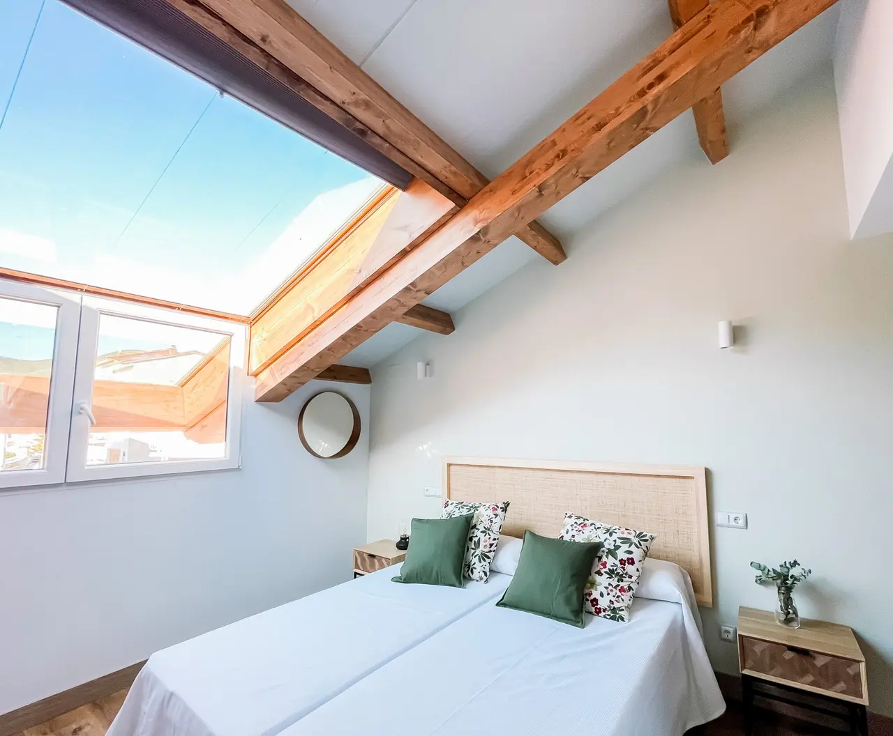 Habitación con cama doble, cabecero de madera, cojines verdes y florales, mesitas de noche, vigas de madera