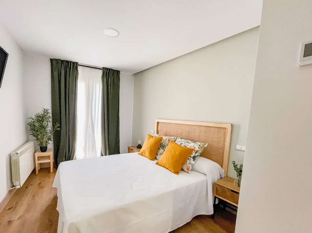 Habitación con cama doble, cabecero de madera, cojines naranjas y florales, mesitas de noche, ventana con cortinas