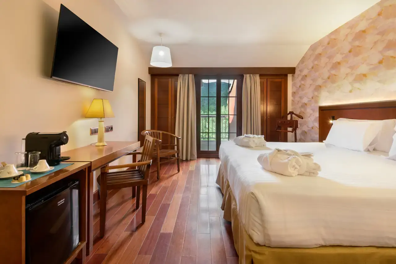 Habitación de hotel con cama doble grande vestida de blanco, escritorio de madera con cafetera y minibar, silla